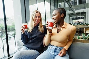 Two people sitting on a bench with coffee cups