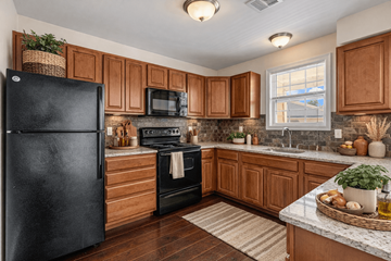 Harrisburg apartment for rent - A black fridge sits in a kitchen with wooden cabinets and a stone backsplash.