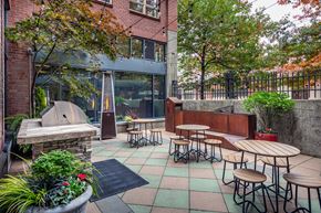 Seattle apartment for rent - A patio with tables and chairs is surrounded by trees.
