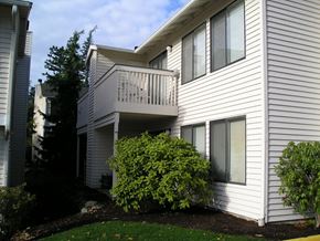Seattle apartment for rent - A white house with a balcony and bushes in front.