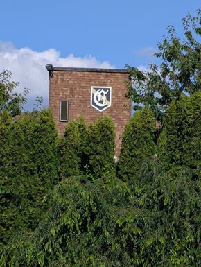 Shoreline apartment for rent - A building with a white emblem on a brick wall surrounded by green trees.