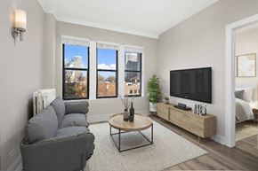Chicago apartment for rent - A living room with a grey couch, a coffee table, a flat screen TV and a window with a view of the city.
