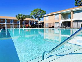 Fort Walton Beach apartment for rent - A swimming pool in front of a brick building with a tree in the background.
