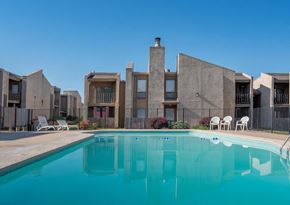Wichita apartment for rent - A swimming pool in front of a building with a clear blue sky.