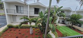 Cocoa Beach apartment for rent - A white building with a balcony and a palm tree in front.