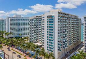 Miami Beach apartment for rent - A large white building with many windows is surrounded by palm trees.