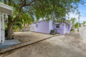Miami triplex for rent - A purple house with a white fence and a tree in front.