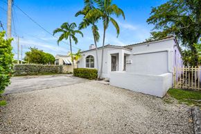 Miami triplex for rent - A white house with a gravel driveway and a gate.