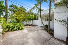 Miami triplex for rent - A white house with a concrete driveway surrounded by greenery.