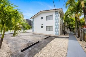 Miami apartment for rent - A white house with a blue patterned wall is surrounded by palm trees.