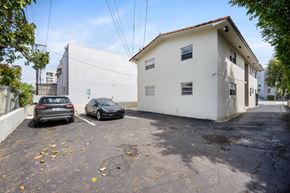 Miami apartment for rent - Two cars are parked in a parking lot in front of a white building.