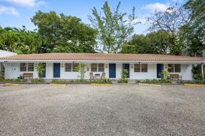 Miami apartment for rent - A white building with blue doors and windows is surrounded by trees.