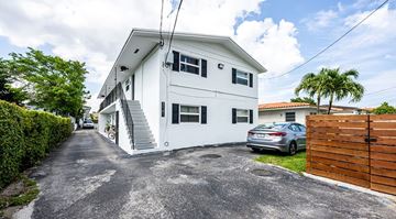 Miami apartment for rent - A white two-story house with a grey driveway and a wooden fence.