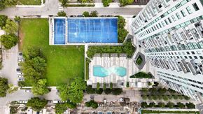 Miami apartment for rent - A large swimming pool is surrounded by a grassy area and a tennis court.