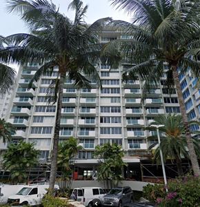 Miami Beach apartment for rent - A large white building with balconies is surrounded by palm trees.