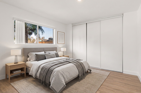 El Cajon apartment for rent - A bedroom with a large bed and a window showing a view of a palm tree.
