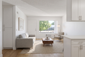 Ramona apartment for rent - A living room with a grey couch, a coffee table, and a window with a view of trees and buildings outside.