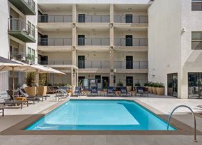 North Hollywood apartment for rent - A large swimming pool is surrounded by lounge chairs and umbrellas in front of a multi-story apartment building.