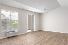 Portland apartment for rent - A room with a slanted ceiling, a window with blinds, a wall-mounted air conditioning unit, and a wooden floor.