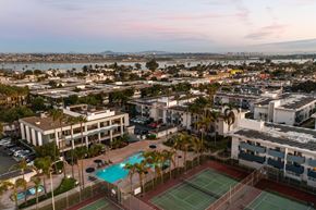 San Diego apartment for rent - A tennis court is surrounded by a pool and palm trees in a residential area.