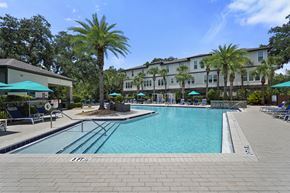 Tampa apartment for rent - A large swimming pool surrounded by a brick patio and palm trees.