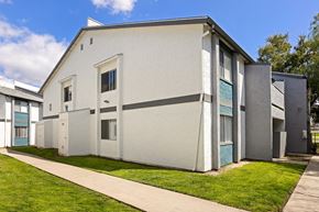 Ramona apartment for rent - A white building with a grey roof and a green lawn in front.