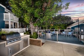 Los Angeles apartment for rent - A patio with a grill and chairs is surrounded by trees.