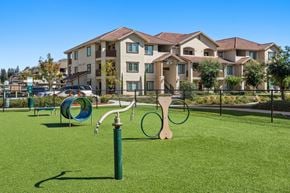 Stockton apartment for rent - A playground with a green slide and a wooden swing set in front of apartment buildings.