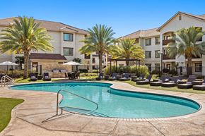 Stockton apartment for rent - A swimming pool surrounded by palm trees and lounge chairs in front of a building.