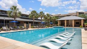 San Antonio apartment for rent - A large swimming pool with lounge chairs and umbrellas in front of a building.