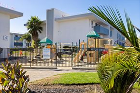 San Diego apartment for rent - A playground with a slide and a green canopy is surrounded by a fence and a building with a number 4 on it.
