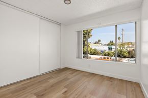 National City apartment for rent - A room with white walls and wooden flooring with a window showing a view of a street with cars and trees.