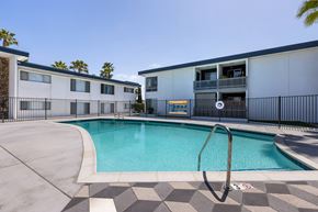 San Diego apartment for rent - A swimming pool in front of a building with a black fence around it.