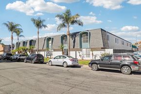 El Cajon apartment for rent - A parking lot with cars and a building with palm trees in the background.