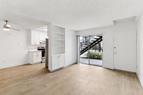 El Cajon apartment for rent - A room with a wooden floor and white walls, with a kitchen area and a staircase visible through the glass door.