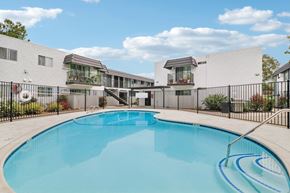 El Cajon apartment for rent - A swimming pool in front of a white building with a black fence around it.