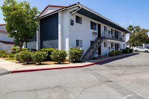 Ramona apartment for rent - A white building with a red tile roof and a parking lot in front.
