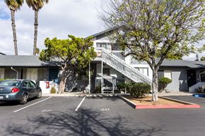 El Cajon apartment for rent - A car is parked in a parking lot in front of a building with a tree.