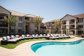 Stockton apartment for rent - A swimming pool is surrounded by lounge chairs and palm trees in front of apartment buildings.