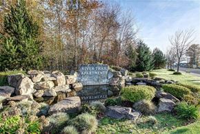 Puyallup apartment for rent - A stone sign for River Trail Apartments sits in front of a grassy area.