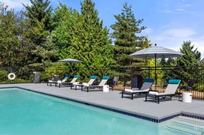 Tumwater apartment for rent - A pool surrounded by trees and chairs under an umbrella.