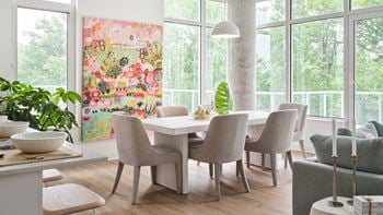 A dining room with a table and chairs and a painting on the wall.