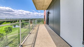 A balcony with a glass railing overlooking a green landscape.