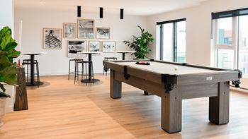 A pool table is in the middle of a room with a plant and a picture frame on the wall.