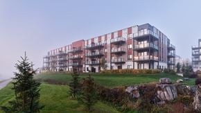 Ottawa apartment for rent - A modern building with red and white balconies is surrounded by a grassy area and a stone wall.