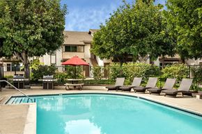 Orange apartment for rent - A pool surrounded by trees and chairs.