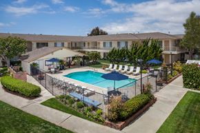 Huntington Beach apartment for rent - A swimming pool surrounded by a fence and umbrellas in a residential area.