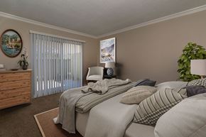 Anaheim apartment for rent - A bedroom with a bed, pillows, a nightstand, a plant, and a window with blinds.