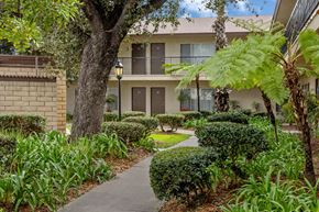 Garden Grove apartment for rent - A building with a balcony is surrounded by green plants.
