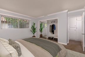 Fountain Valley apartment for rent - A bedroom with a bed, pillows, a window, a coat rack, and a plant.